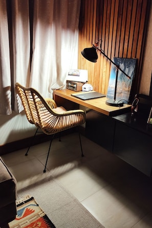 Een moderne werkruimte met een houten bureau, een rieten stoel, een bureaulamp en een computer beeldscherm.