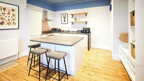 A kitchen with a central island, bar stools, a microwave, and a hanging plant. - Host and Stay | Balmoral Terrace (Saltburn-by-the-Sea)