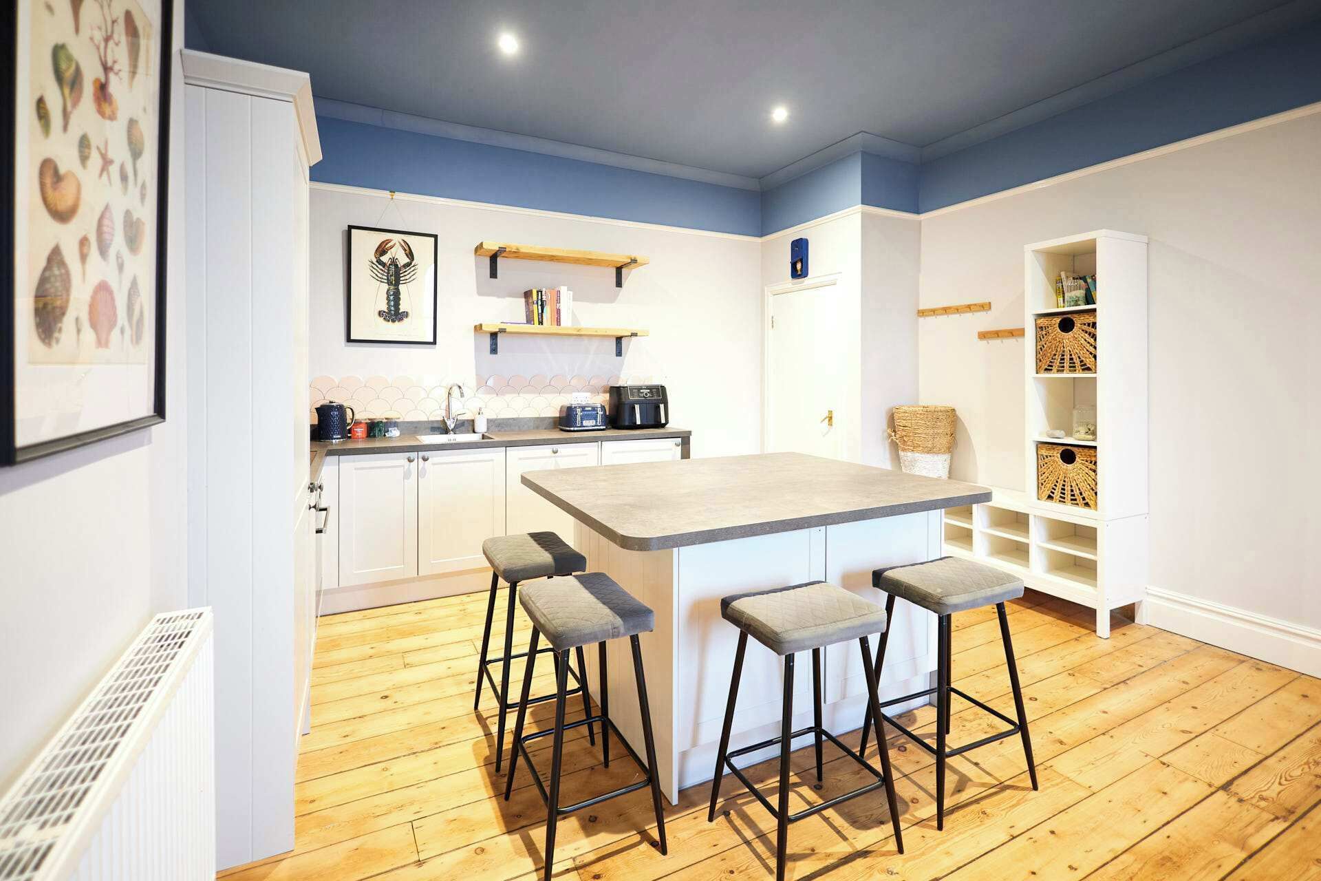 Une cuisine moderne dotée d’un îlot central, de tabourets de bar, d’un plancher en bois et de meubles de cuisine blancs.