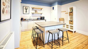 A modern kitchen with a central island, bar stools, wooden flooring, and a white cabinetry design. - Host and Stay | Balmoral Terrace (Saltburn-by-the-Sea)