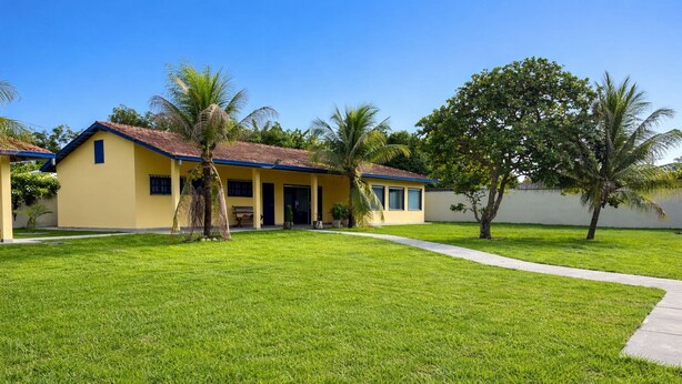 A yellow building with a red roof, surrounded by a well-maintained lawn and palm trees. - Casa ampla com jardim e 3 suítes em Novo Airão (Novo Airão)