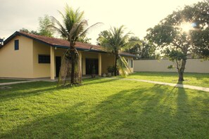 A single-story building with a flat roof, a covered porch, and a well-maintained lawn with a few palm trees. - Casa ampla com jardim e 3 suítes em Novo Airão (Novo Airão)