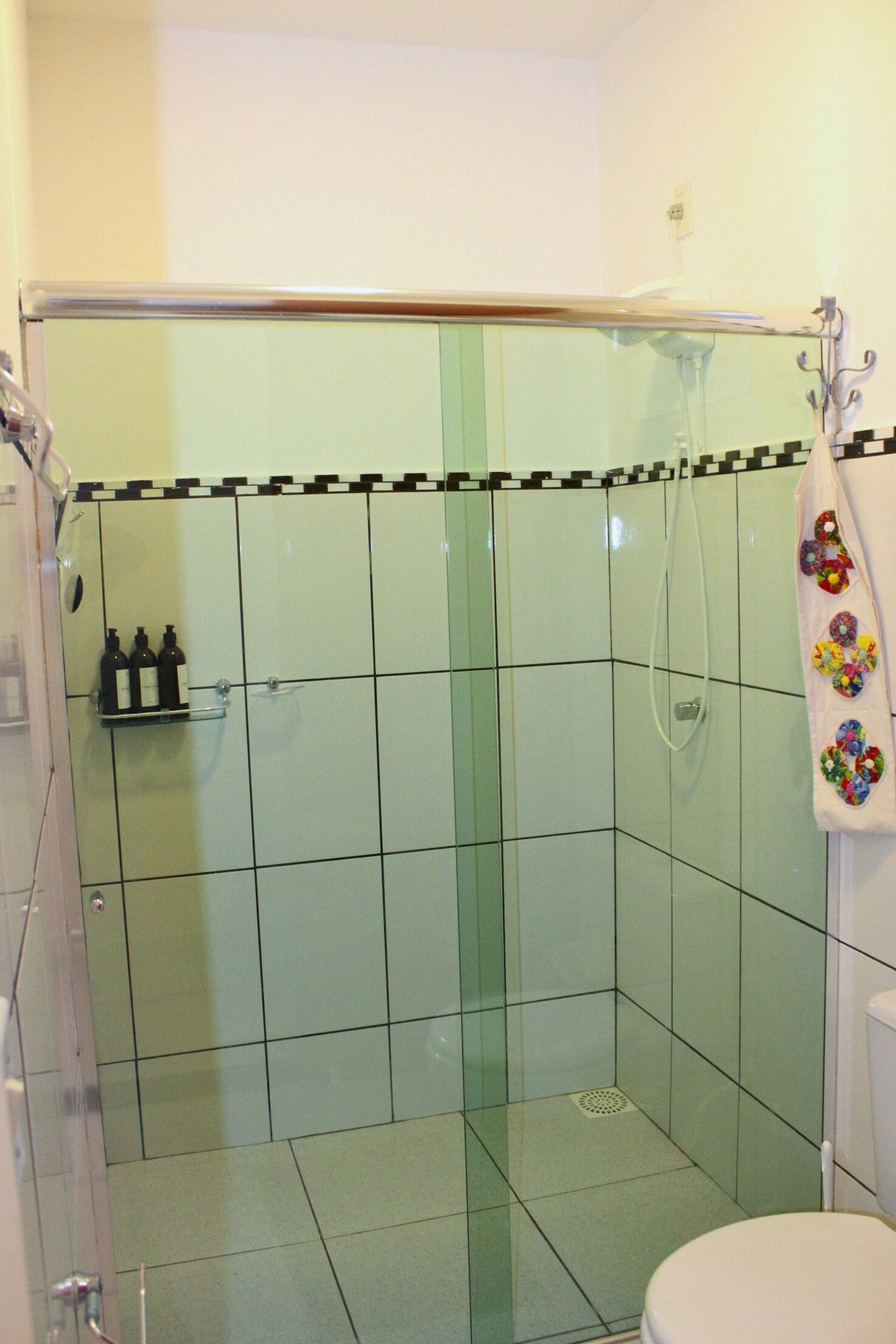 A bathroom with a glass-enclosed shower, a toilet, and a shelf with toiletries.