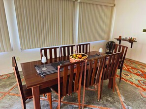 A dining area with a wooden table and chairs, a fruit basket, a fan, and a patterned rug. - Casa ampla com jardim e 3 suítes em Novo Airão (Novo Airão)