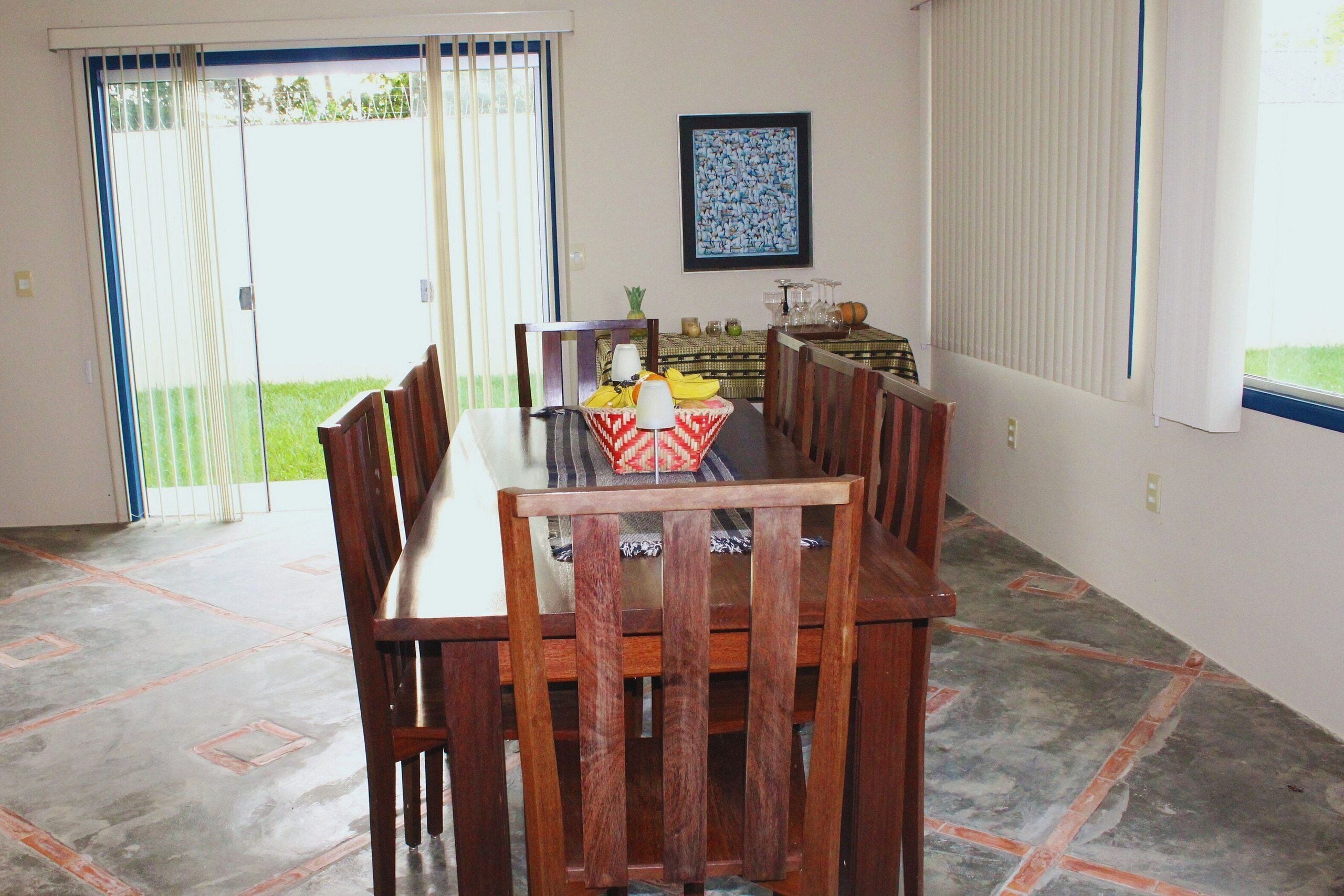 Uma área de refeições com mesa e cadeiras, um quadro na parede e vista pela porta de vidro deslizante.