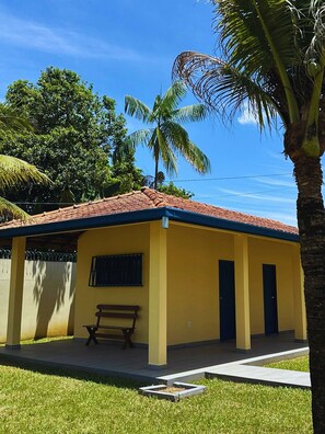A yellow building with a red roof, a bench, and a palm tree. - Casa ampla com jardim e 3 suítes em Novo Airão (Novo Airão)
