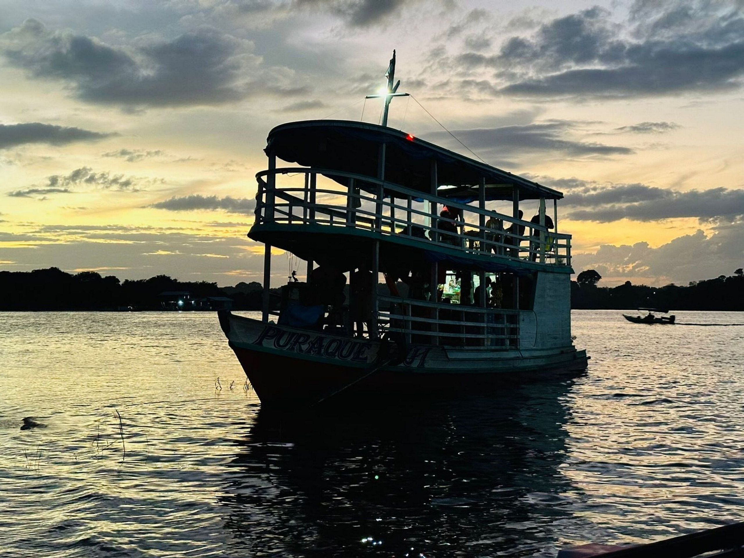 A boat with a name 'PURAQUE' on its side, a covered upper deck, and a flag on top.