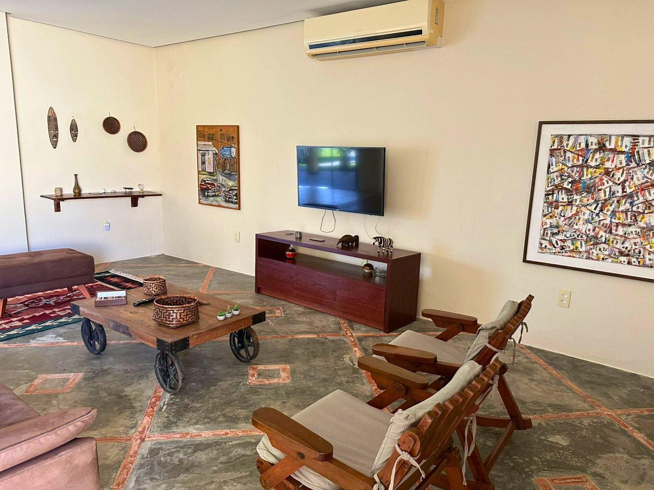 Uma sala de estar com televisão, mobiliário de madeira, um sofá e objetos decorativos.