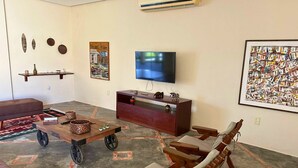 A living room with a TV, wooden furniture, a sofa, and decorative items. - Casa ampla com jardim e 3 suítes em Novo Airão (Novo Airão)