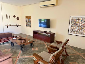 A living room with a TV, wooden furniture, a sofa, and decorative items. - Casa ampla com jardim e 3 suítes em Novo Airão (Novo Airão)