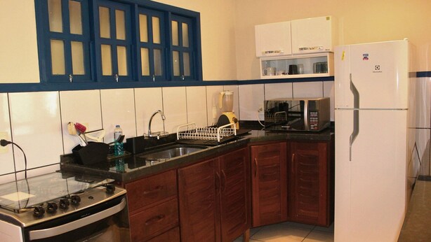 A kitchen with a stove, sink, microwave, refrigerator, and wooden cabinets. - Casa ampla com jardim e 3 suítes em Novo Airão (Novo Airão)