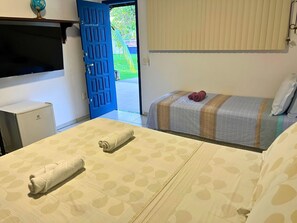 A hotel room with two beds, a TV, a desk, and a door leading outside. - Casa ampla com jardim e 3 suítes em Novo Airão (Novo Airão)