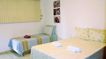 Quarto de hotel com duas camas, uma janela com persianas e três quadros na parede.