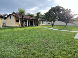 A building with a red-tiled roof, a covered porch, and a well-maintained lawn. - Casa ampla com jardim e 3 suítes em Novo Airão (Novo Airão)