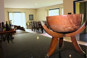 Un espace repas avec une table et des chaises, un bar avec des bouteilles et une grande fenêtre avec des rideaux.
