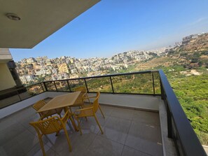 Varanda com mesa e cadeiras, proporcionando vista para o horizonte urbano com edifícios e áreas verdes.
