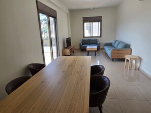 Ein modernes Wohnzimmer mit einem Holzesstisch, zwei Sofas, einem Fernseher und einer kleinen Holzkommode.
