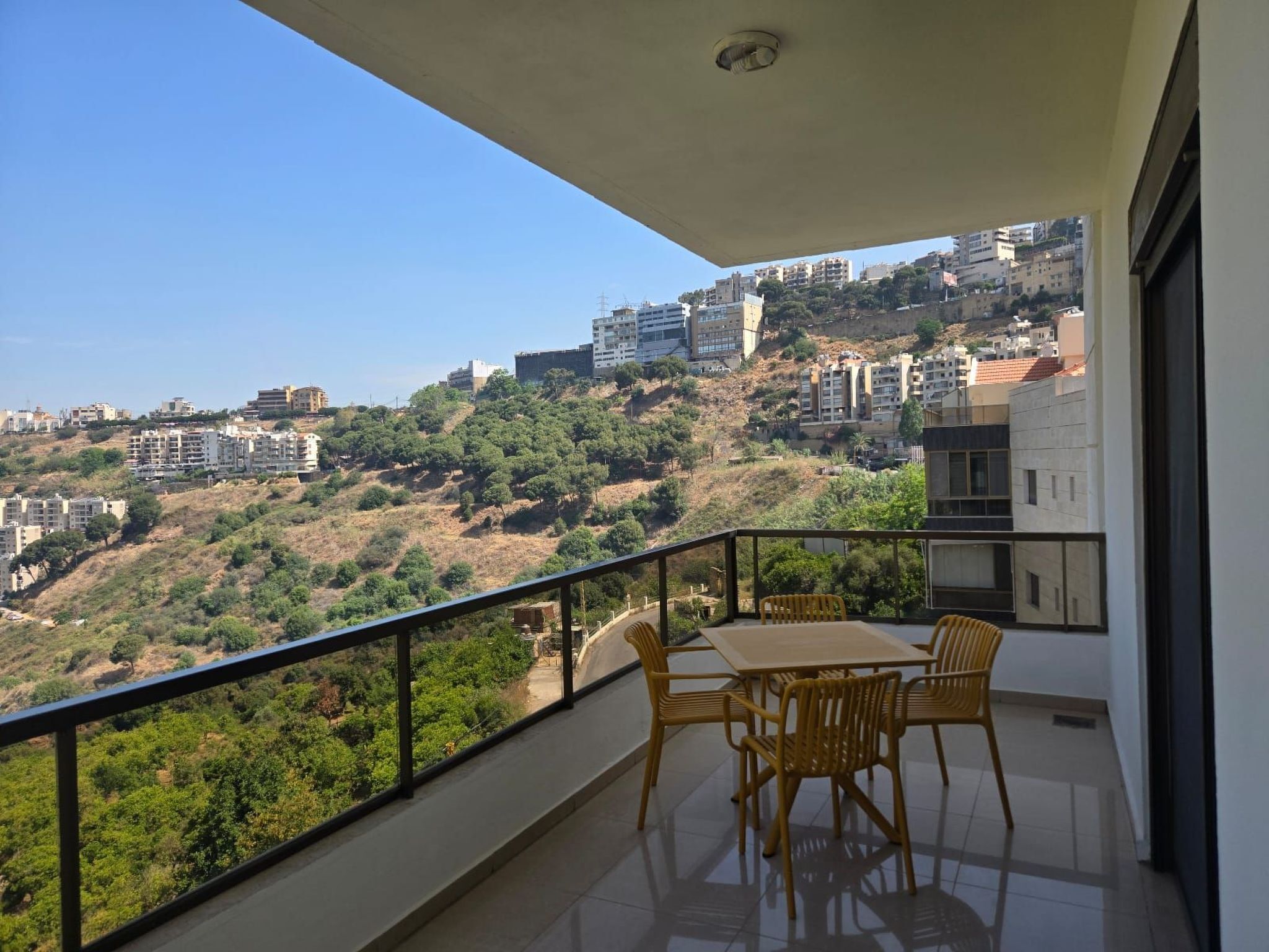 A balcony with a table and chairs, overlooking a hillside with buildings.