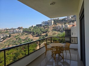 Uma varanda com mesa e cadeiras, com vista para uma encosta com edifícios.