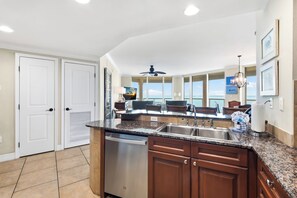 A kitchen with a granite countertop, stainless steel sink, and wooden cabinets. - 🏖️Sound and Gulf Views From Every Room | Resort Amenities | Portofino 4-1101 (Pensacola Beach)