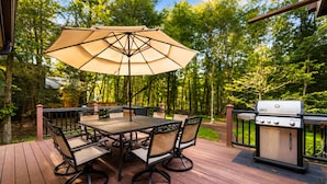 Une terrasse extérieure avec une table et des chaises, un barbecue et un parasol.
