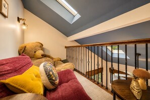 A cozy room with a large teddy bear, a red couch, and a staircase with a wooden railing. - Lake Naomi, Fairy Village, Firepit | Creekside Cabin (Pocono Pines)