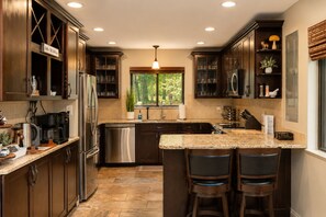 A modern kitchen with dark wood cabinets, stainless steel appliances, a granite countertop, and a window with a view of greenery. - Lake Naomi, Fairy Village, Firepit | Creekside Cabin (Pocono Pines)