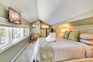 Ein Hotelzimmer mit einem Bett, einem Sessel, einem Schreibtisch mit Kaffeemaschine, einem Ventilator und einem Fernseher, der einen Kamin zeigt.