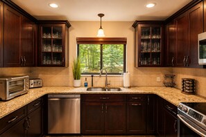 A kitchen with dark wood cabinets, a stainless steel dishwasher, a built-in oven, and a window with a view of greenery. - Lake Naomi, Fairy Village, Firepit | Creekside Cabin (Pocono Pines)