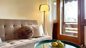 A cozy living room with a sofa, a glass coffee table with a bowl of fruit, a lamp, and a view through a window. - Nature Escape in Aeschi – Close to Interlaken (Aeschi bei Spiez)