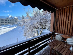 A wooden balcony with a view of a snow-covered landscape and buildings.