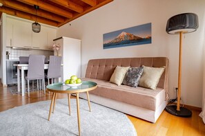 A living room with a sofa, a round glass table with apples, a painting of a mountain, and a floor lamp.