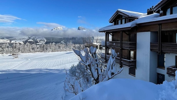 A snow-covered landscape with a building featuring a balcony and a view of distant mountains. - Nature Escape in Aeschi – Close to Interlaken (Aeschi bei Spiez)