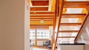A corridor with wooden beams, a ceiling fan, and a view of an apartment building through large windows. - Nature Escape in Aeschi – Close to Interlaken (Aeschi bei Spiez)