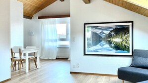 Ein modernes Wohnzimmer mit einem großen, gerahmten Landschaftsbild, einem Essbereich mit weißer Möbel und einer Holzziel.