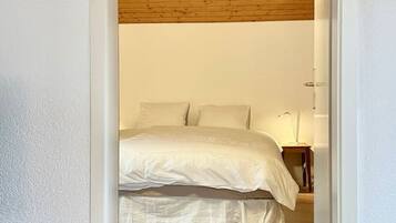 A bedroom with a wooden ceiling, a bed with white bedding, and a nightstand with a lamp.