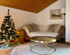 A cozy living room with a Christmas tree, a round coffee table, a sofa, and a painting on the wall. - Relaxed Loft Stay Between Lake & Mountains (Leissigen)