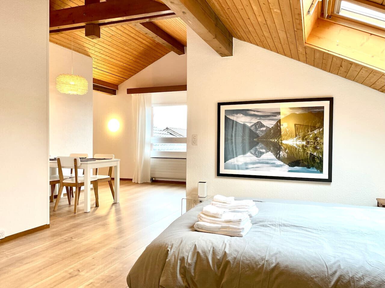 Une chambre d’hôtel avec un lit, une table à manger avec des chaises, un tableau au mur et une fenêtre avec des rideaux.