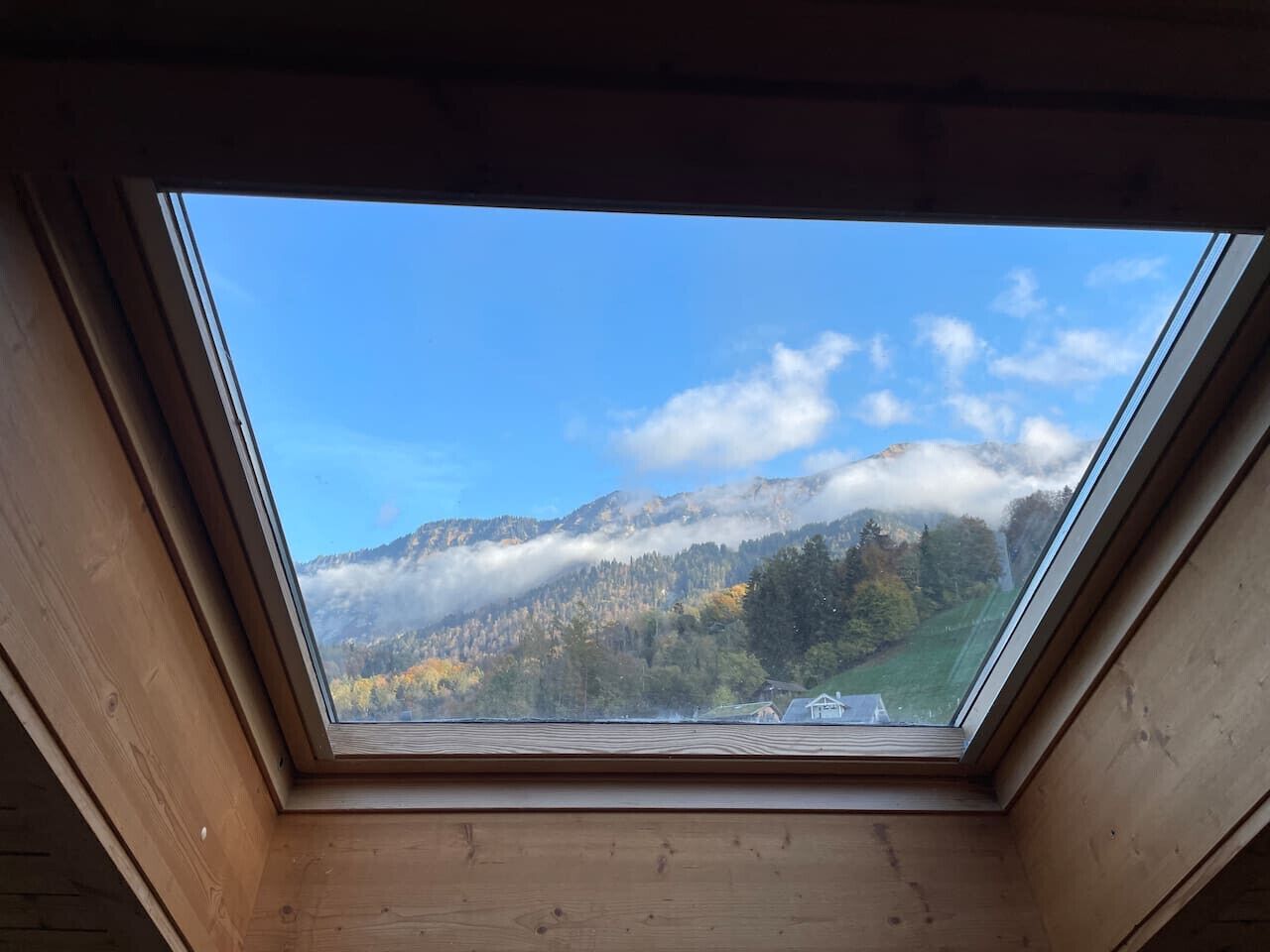 A skylight with a view of a mountainous landscape and a small building in the distance.