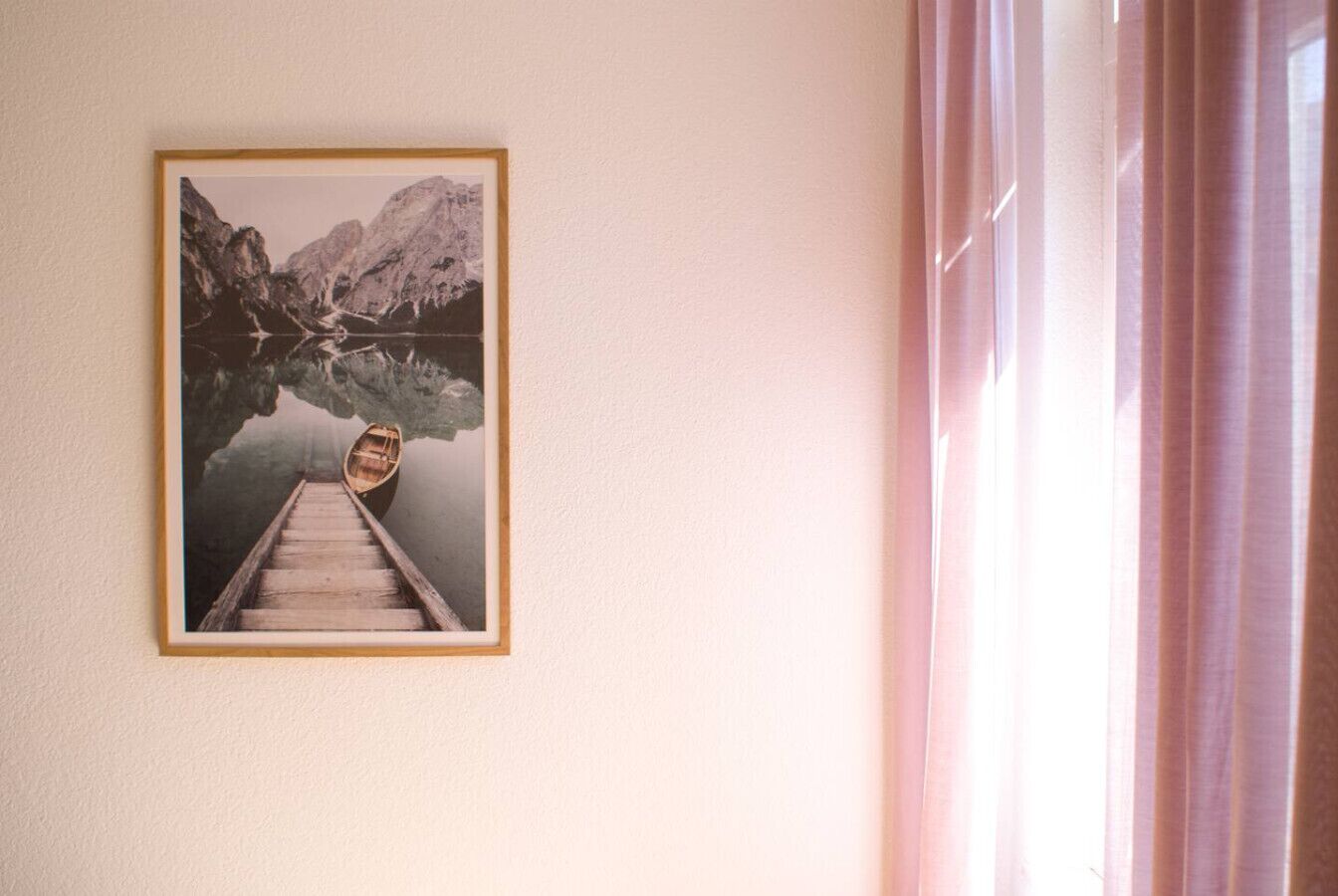 Een lijst met een foto van een bergmeer, met een houten pad dat naar een boot leidt, hangend aan een effen muur.