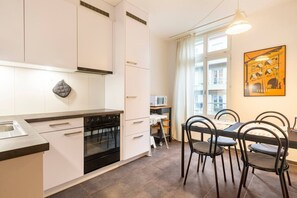 A modern kitchen with white cabinets, a black stove, and a dining area with a table and chairs.