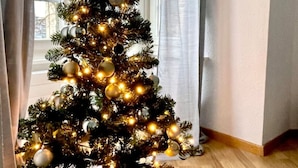 Un sapin de Noël décoré de guirlandes lumineuses et d’ornements, dans une pièce avec une fenêtre et des rideaux.