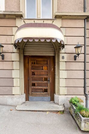 A building with a wooden door, a number '8' above it, and a small garden area with plants to the right.