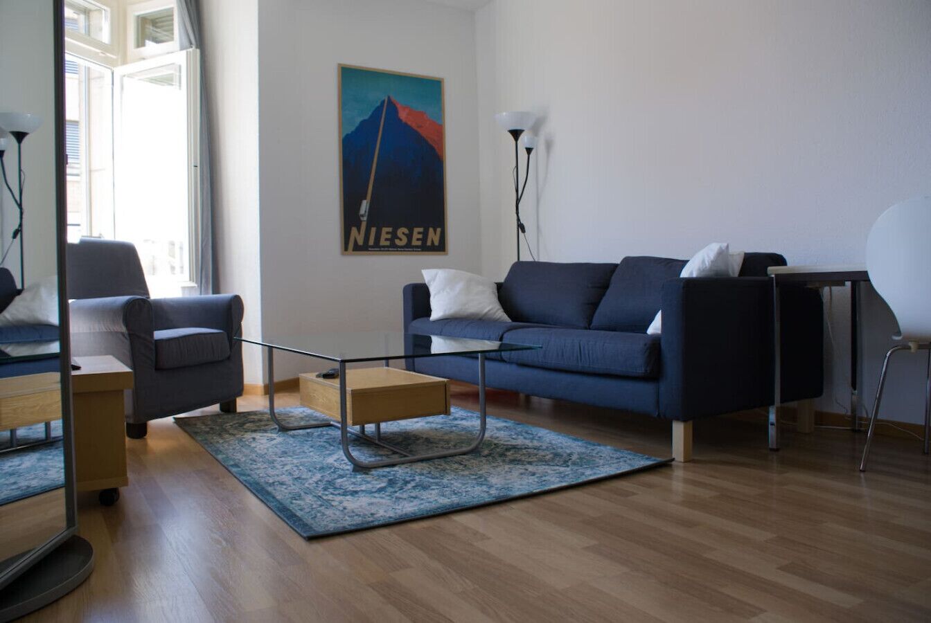 A modern living room with a blue sofa, a glass coffee table, and a wooden side table.