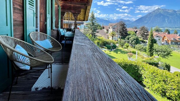 Ein Holzbalkon mit Korbstühlen und einem Tisch, mit Blick auf eine gebirgige Landschaft.