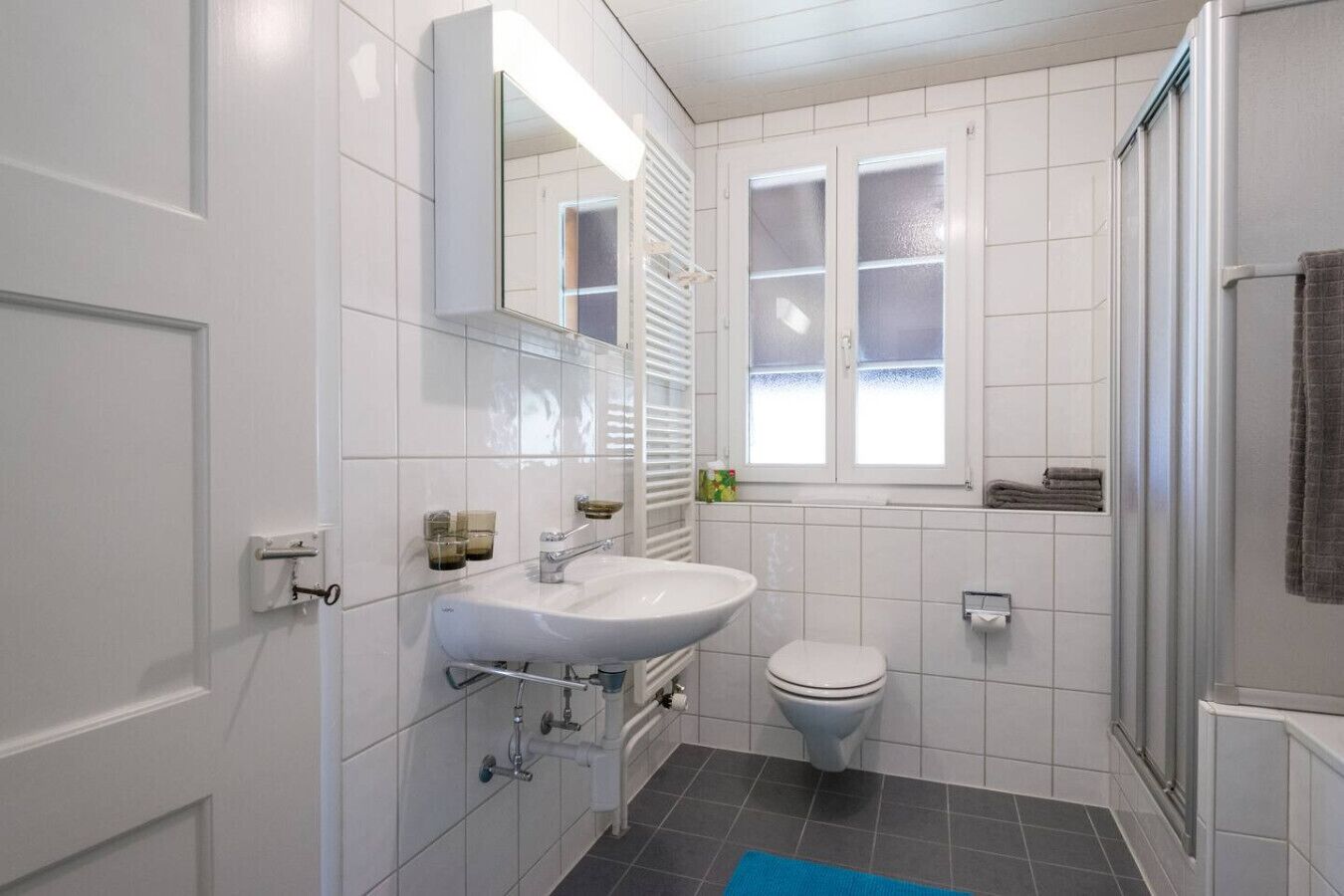 Ein modernes Badezimmer mit Waschbecken, Toilette und Dusche, alles in Weiß.