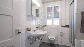 Ein modernes Badezimmer mit Waschbecken, Toilette und Dusche, alles in Weiß.