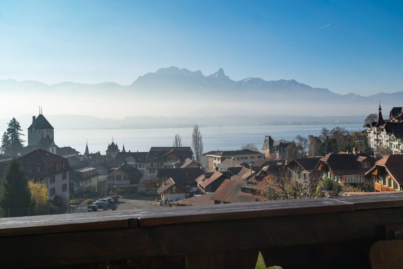 Une ville à l’architecture traditionnelle, avec un clocher d’église imposant, et offrant une vue sur les montagnes et un lac.