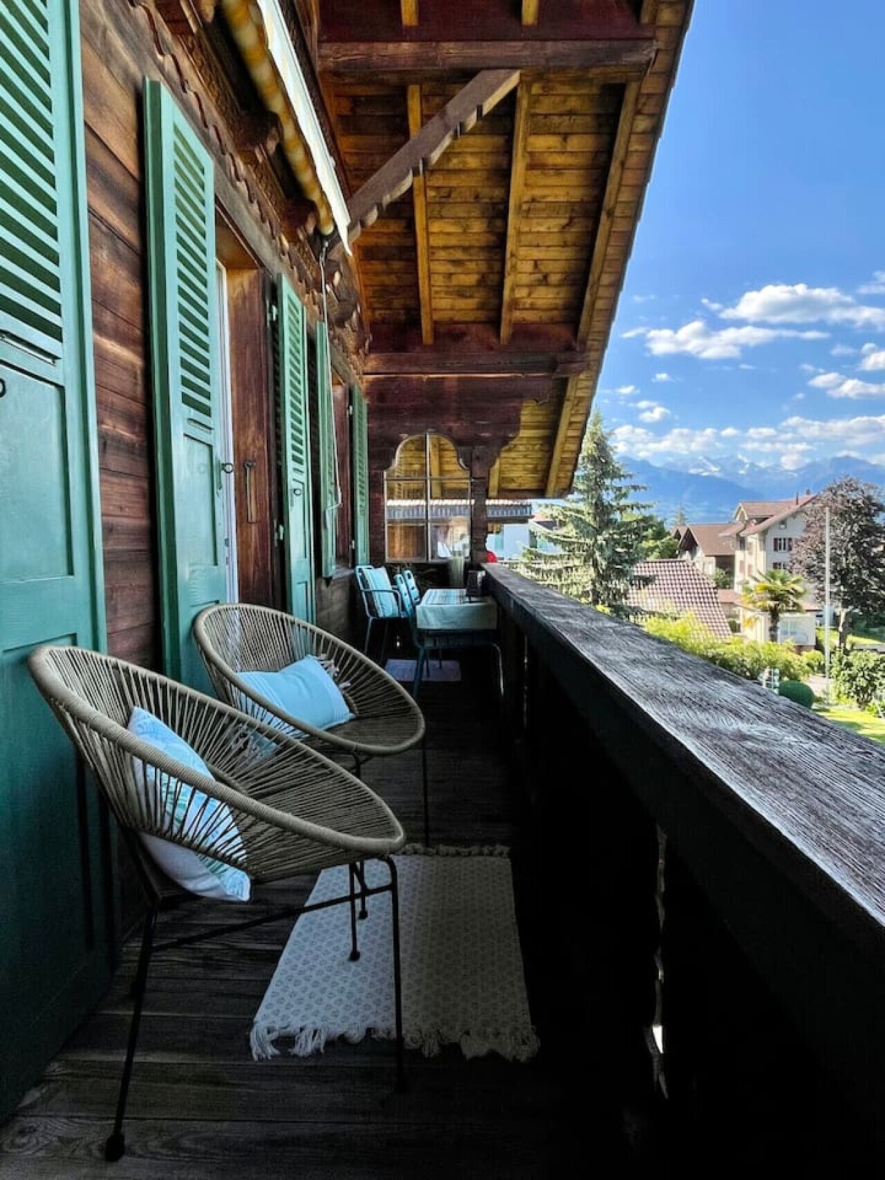 Ein Holzbalkon mit Korbstühlen und Blick auf Häuser und Berge.