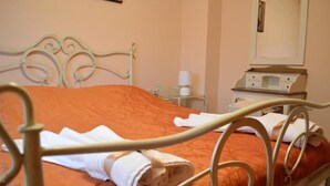 A bed with an orange bedspread and white towels, a bedside table with a lamp, and a small dresser with a mirror. - Angellinas Apartment (Chania)